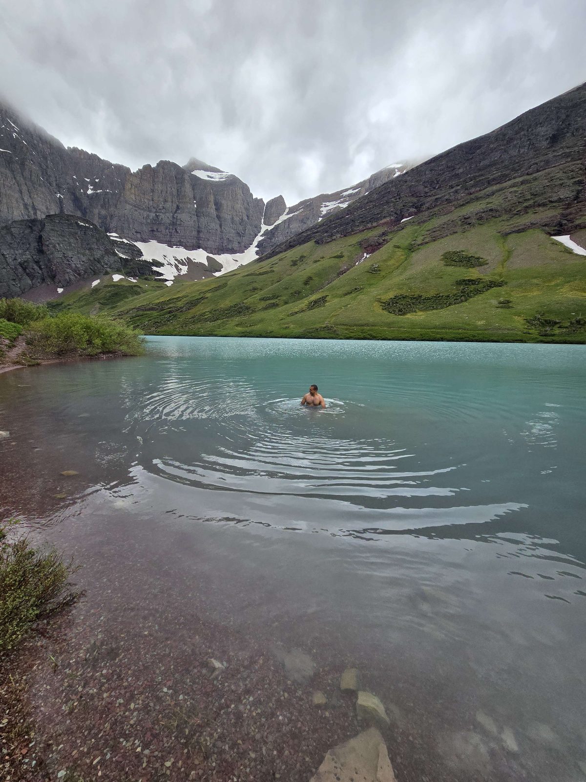 Swimming in a turquoise glacial lake below a cirque of snow-streaked mountains.