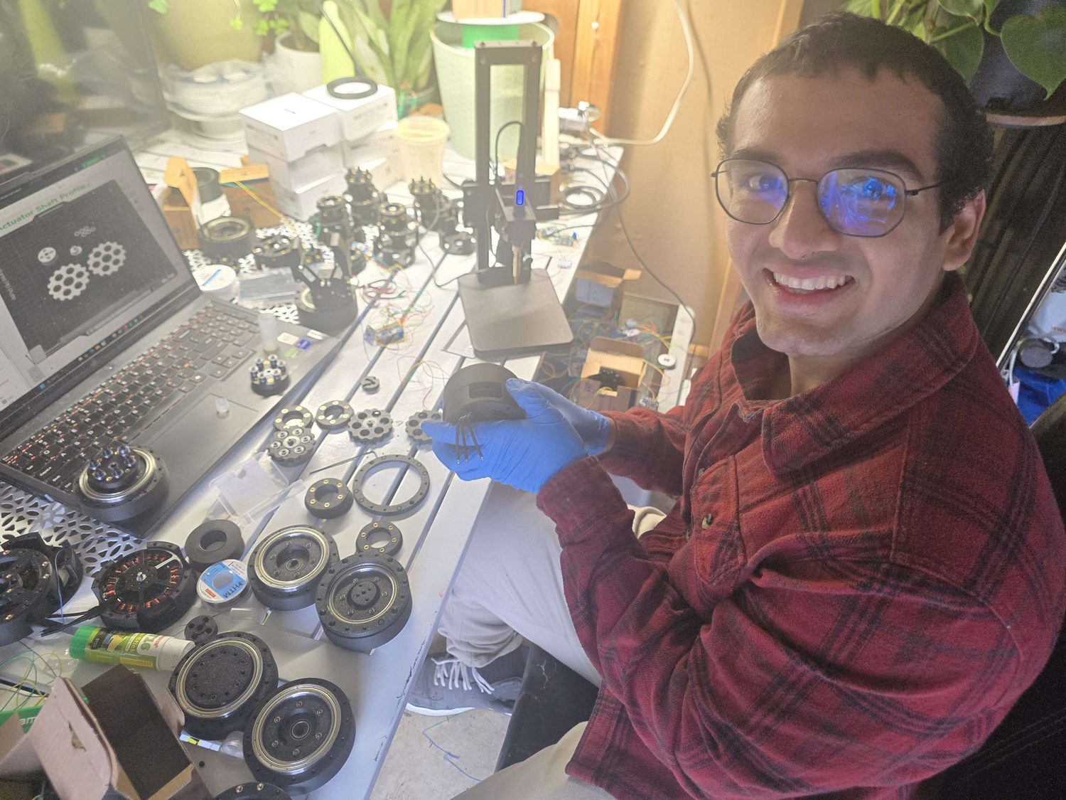 Jose at the bench holding an actuator housing, with rotors, bearings and gear plates laid out.