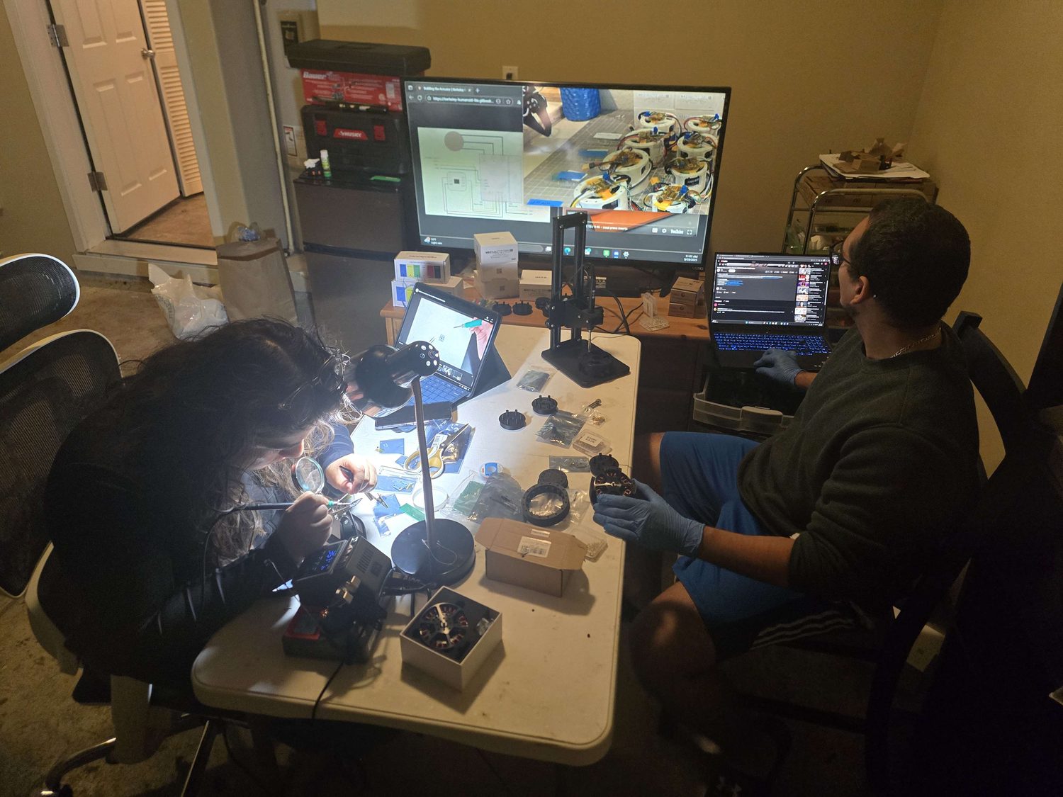 Two people soldering encoder boards at the bench.