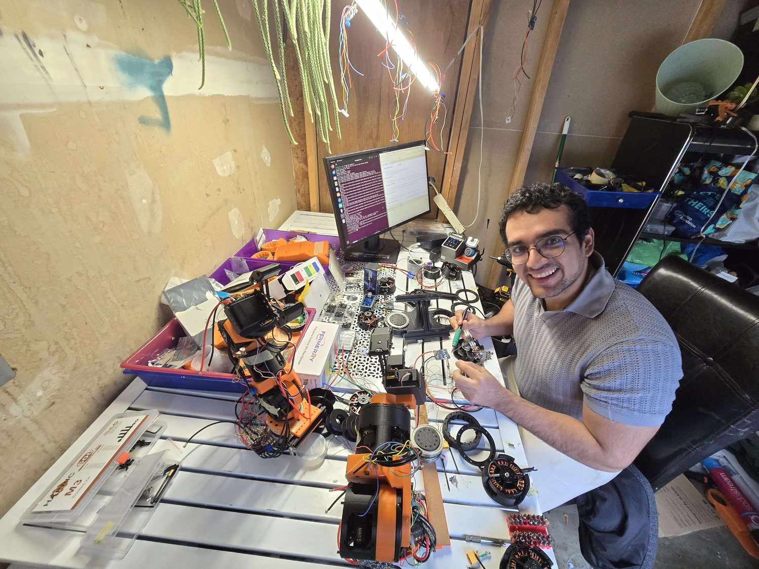 Jose assembling an arm at the bench, with printed limb sections and motors around him.