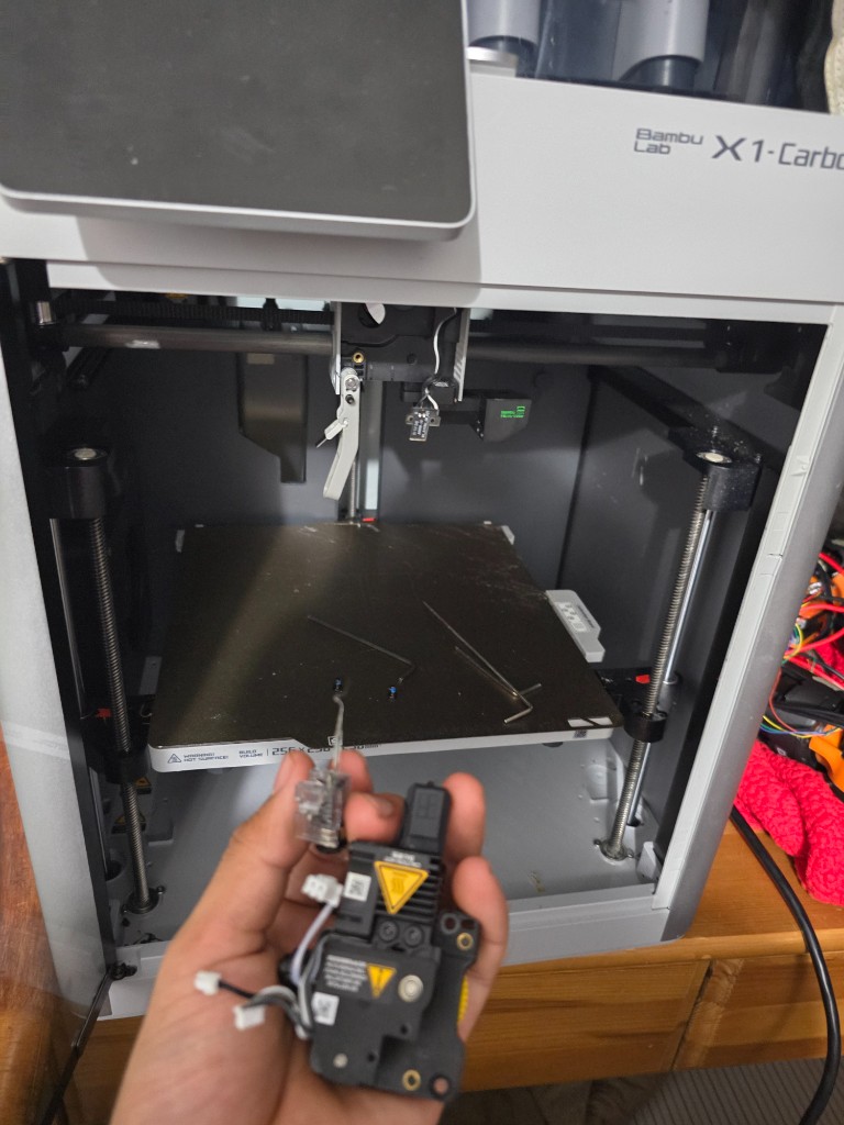 Open Bambu Lab X1-Carbon with the hotend in hand and tools on the build plate.