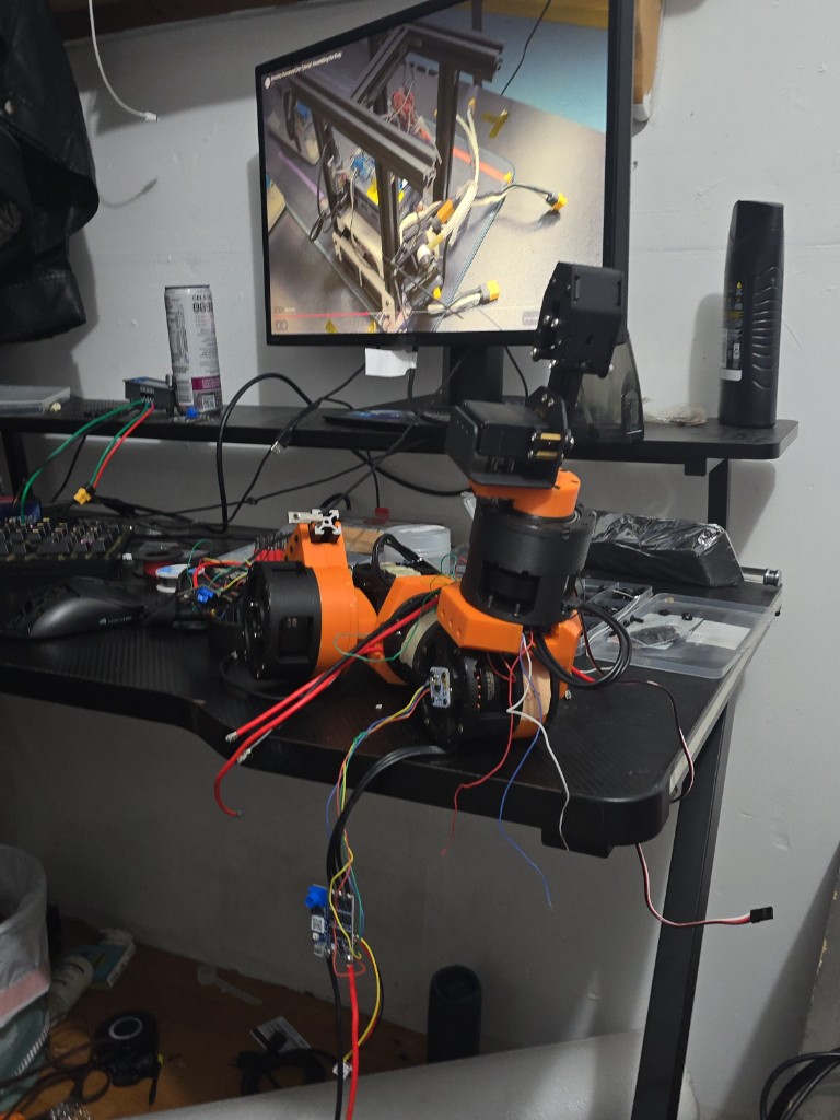 Assembled orange humanoid arm with exposed wiring next to a monitor on the desk.