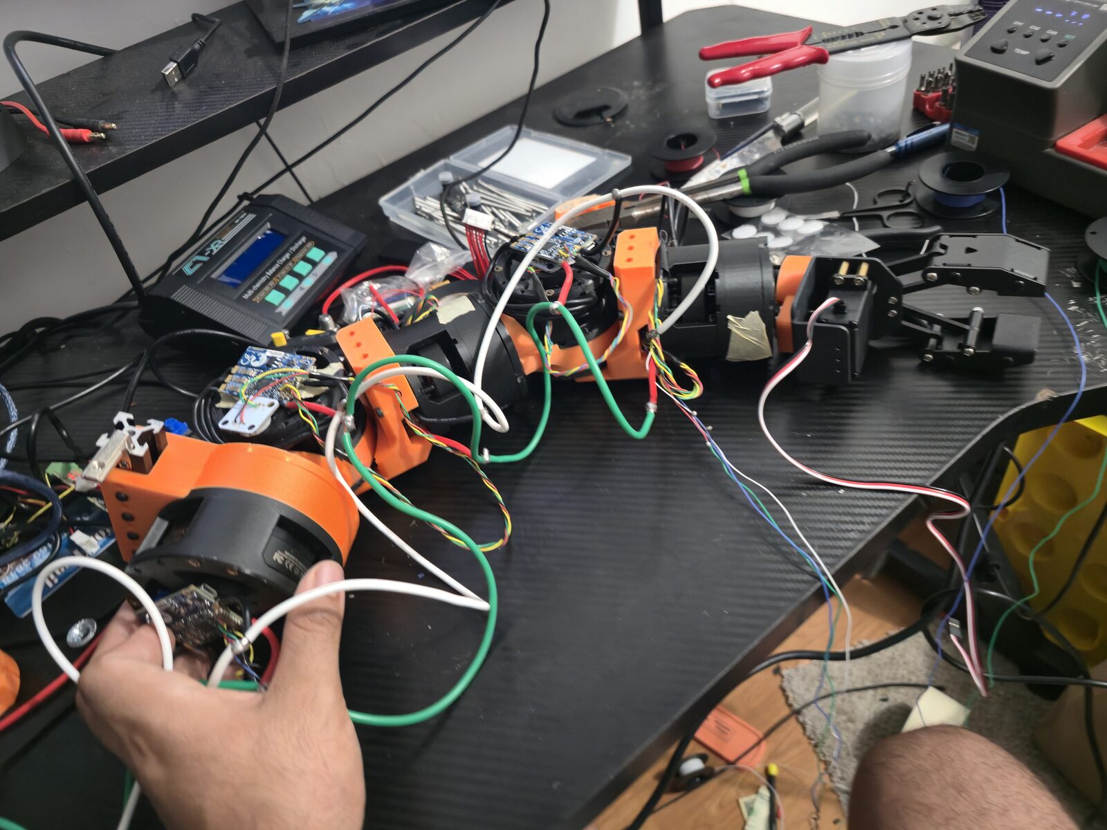 Humanoid arm on the bench with white and green wiring being dressed, tools around it.