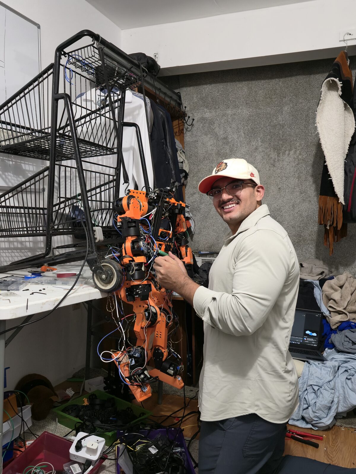 Jose kneeling beside the hanging orange humanoid, resoldering a disconnected motor.